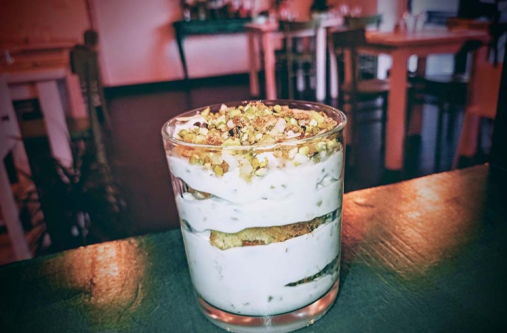 Dolce al bicchiere a strati con crema chiara e granella di pistacchi.