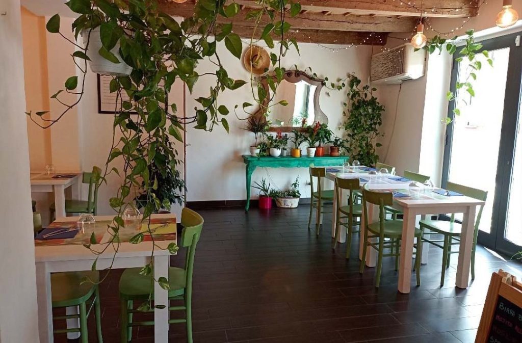La sala del Green Corner: tavoli chiari, sedie verdi, travi a vista e piante sospese.